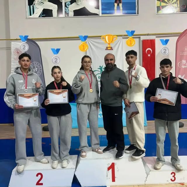 Çetinkaya Fight Club sporcuları madalyalarıyla kürsüde, ortada antrenör Erdal Çetinkaya